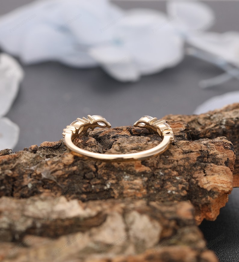 May include: A gold ring with a delicate design featuring small round stones set in a curved band. The ring is shown on a piece of wood.