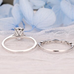 Puede incluir: Un conjunto de anillos de compromiso de plata con una piedra central grande de forma ovalada y piedras m&aacute;s peque&ntilde;as alrededor de la banda. La banda de boda tiene un dise&ntilde;o delicado con peque&ntilde;as piedras engastadas en un patr&oacute;n curvo.