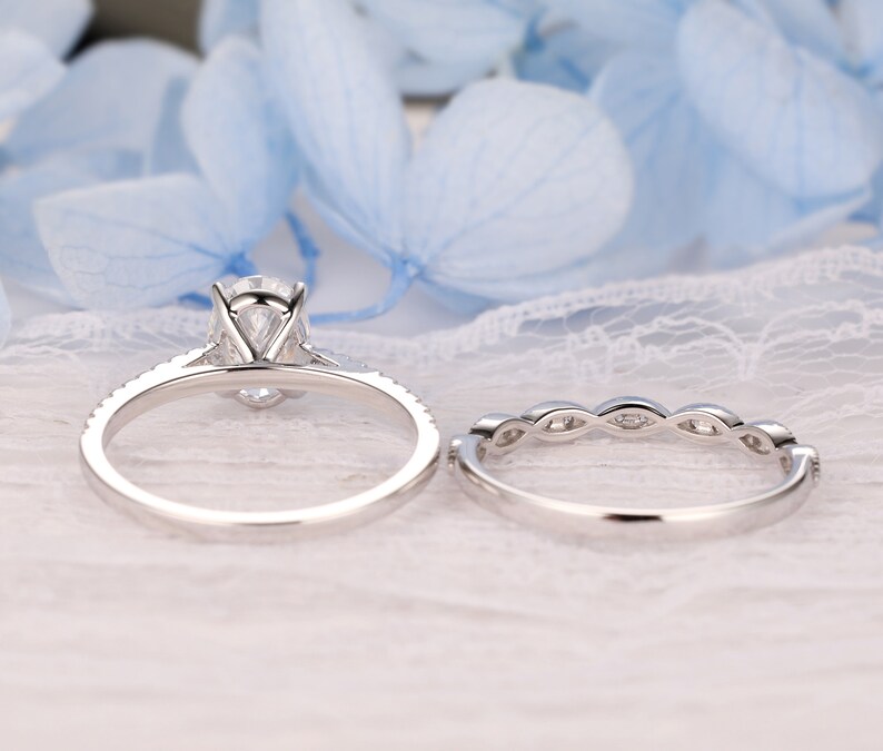 Puede incluir: Un conjunto de anillos de compromiso de plata con una piedra central grande de forma ovalada y piedras m&aacute;s peque&ntilde;as alrededor de la banda. La banda de boda tiene un dise&ntilde;o delicado con peque&ntilde;as piedras engastadas en un patr&oacute;n curvo.