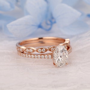 Puede incluir: Un anillo de compromiso de oro rosa con una gran piedra central ovalada y una banda a juego con un dise&ntilde;o delicado y festoneado.