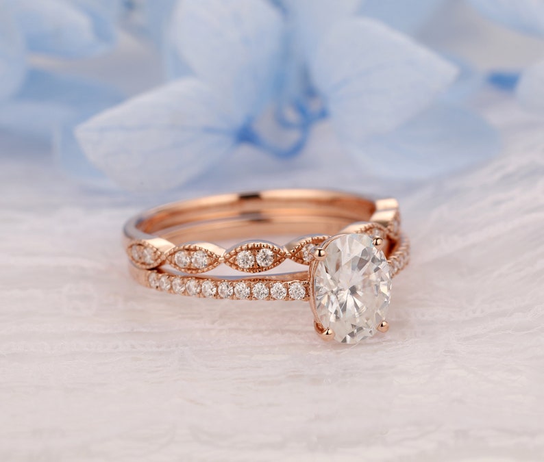 Puede incluir: Un anillo de compromiso de oro rosa con una gran piedra central ovalada y una banda a juego con un dise&ntilde;o delicado y festoneado.