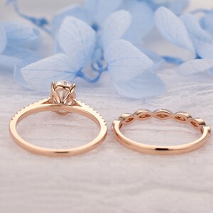 Puede incluir: Un conjunto de anillo de compromiso de oro rosa con una piedra central redonda y una banda a juego con peque&ntilde;as piedras redondas. El anillo est&aacute; sobre un fondo blanco.