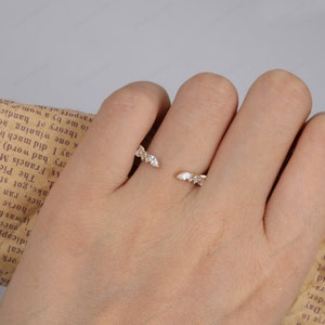 May include: A gold ring with a delicate design featuring multiple small, clear gemstones set in a curved shape. The ring is worn on a finger.