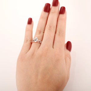 Puede incluir: Un anillo de compromiso de oro rosa con una piedra central ovalada grande y una banda m&aacute;s peque&ntilde;a de diamantes pav&eacute;.