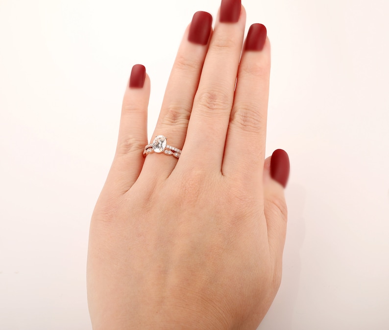 Puede incluir: Un anillo de compromiso de oro rosa con una piedra central ovalada grande y una banda m&aacute;s peque&ntilde;a de diamantes pav&eacute;.