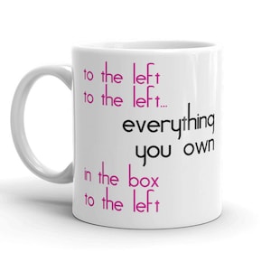 Op de afbeelding: Witte keramische mok met zwarte tekst die "to the left to the left... everything you own in the box to the left" luidt. De tekst "left" is roze.