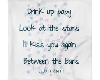 Op de afbeelding: Een wit kussen met een blauw en roze aquarel sterrenpatroon. De tekst "Drink up baby Look at the stars I'll kiss you again Between the bars ELLIOTT SMITH" is op het kussen gedrukt.