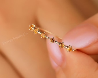 May include: A delicate gold ring with a row of small, round, orange gemstones.