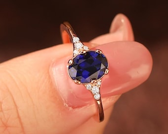 Puede incluir: Un anillo de oro rosa con una gran piedra de zafiro azul ovalada rodeada de piedras pequeñas transparentes.