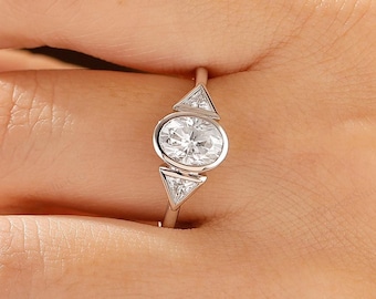 Anillo de compromiso de oro macizo con triple piedra de moissanita ovalada engastada en bisel.