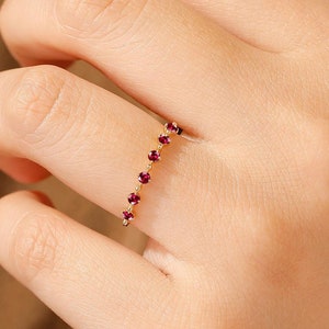 May include: A gold ring with a row of small red gemstones.