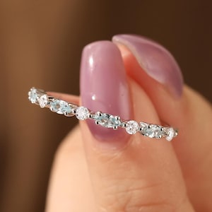 May include: A delicate silver band ring with a row of small, clear and blue gemstones.