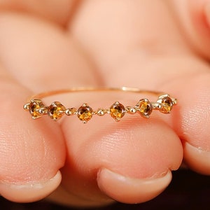 May include: A delicate gold ring with a row of small, round, amber-colored gemstones.