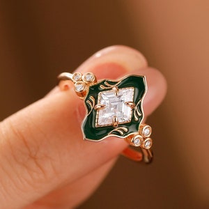 May include: A gold ring featuring a square green enamel setting with a clear, square-cut gemstone. The ring is embellished with small, clear gemstones around the setting.