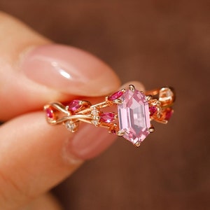 May include: A rose gold ring with a pink gemstone and smaller pink gemstones set in a delicate vine design.