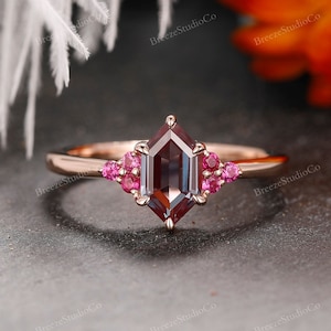 Pode incluir: Anel de noivado em ouro rosa com uma gema hexagonal marrom escura e pedras de acento rosa.