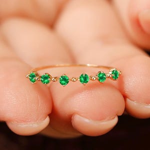 Puede incluir: Un delicado anillo de oro con una fila de seis piedras preciosas de color verde esmeralda.