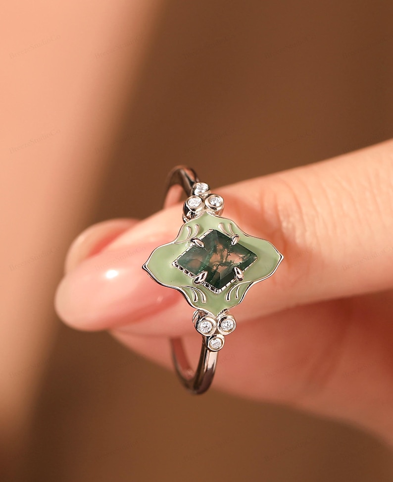 Puede incluir: Anillo de plata con un engaste en forma de hoja verde claro y una piedra cuadrada verde musgo. Peque&ntilde;as piedras redondas y claras est&aacute;n engastadas a cada lado del engaste. Una joya.