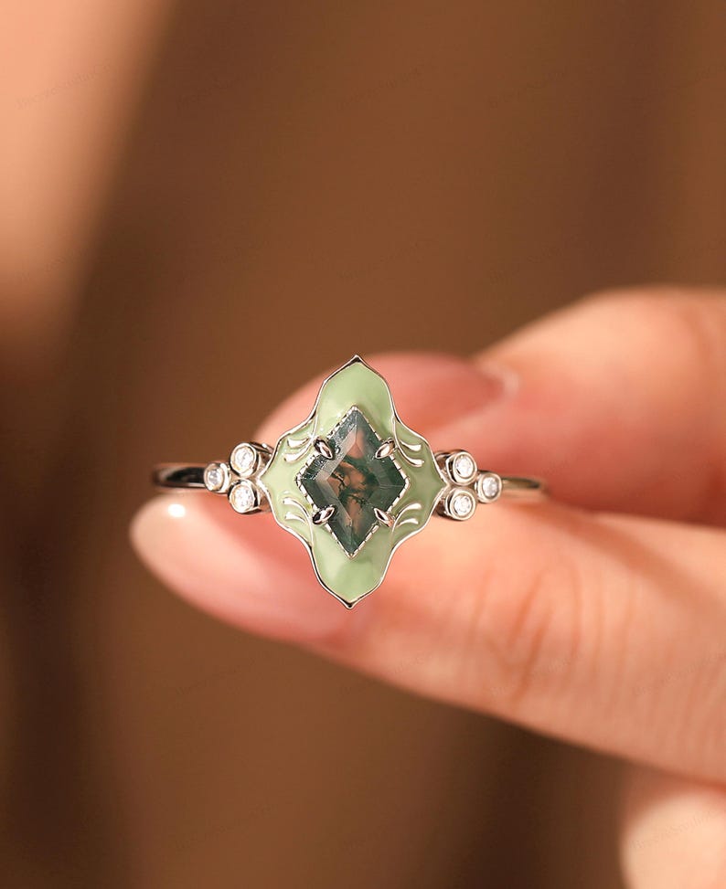Celebrate your love with this exquisite Handcrafted Mint Green Enamel Engagement Bridal Ring, a stunning piece that combines modern charm with retro elegance. This unique ring features a captivating rhombus-cut 6x8mm real moss agate gemstone, celebrated for its enchanting patterns and vibrant hues of green.