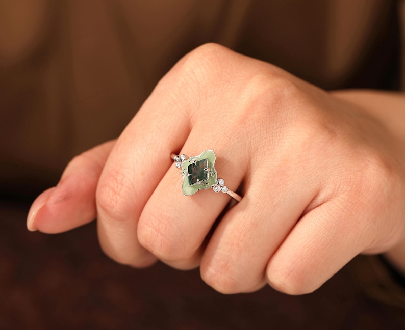 Puede incluir: Un anillo de plata con una piedra verde claro en forma de tr&eacute;bol de cuatro hojas con un centro verde oscuro. El anillo tiene peque&ntilde;as piedras de acento transparentes en la banda y alrededor de la piedra principal.