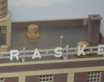 Puede incluir: Un modelo de un edificio de ladrillo con una torre de agua en el techo. El edificio tiene un letrero que dice "KRASKE" en el techo.