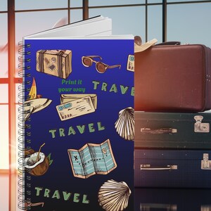 May include: A spiral-bound notebook with a blue cover featuring travel-themed illustrations, including a suitcase, sunglasses, and a map. The text "Print it your way" and "TRAVEL" are also visible. A stack of vintage suitcases is on the right.