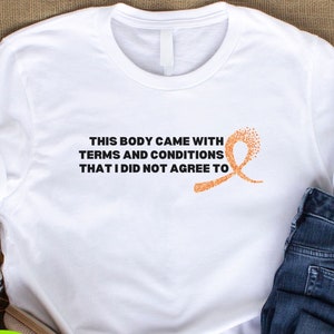 May include: White t-shirt with the text "THIS BODY CAME WITH TERMS AND CONDITIONS THAT I DID NOT AGREE TO" in black. An orange ribbon graphic is to the right of the text. The shirt is next to a pair of blue jeans and a pair of tan shoes.