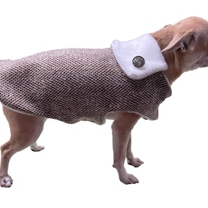 Può includere: Un cappotto per cani in tweed marrone e bianco con un colletto in pelliccia bianca e un bottone argentato. Il cappotto è su un piccolo cane marrone chiaro.