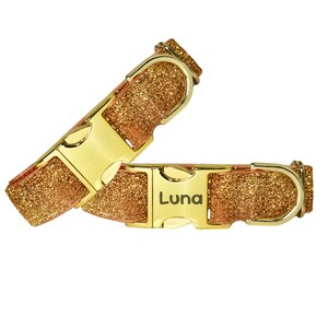 Op de afbeelding: Twee hondenhalsbanden met goudkleurige metalen gespen en glitterende, goudkleurige riemen. Eén halsband is gedeeltelijk losgemaakt en de andere is vastgemaakt met de naam "Luna" op de gesp.