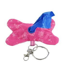 Op de afbeelding: Roze stoffen hondenpoepzakdispenser met een blauwe zakdispenser en een zilveren sleutelhanger. De dispenser is versierd met een wit paardenbloemmotief.