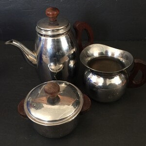 May include: A silver tea set with wooden handles. The set includes a teapot, creamer, and sugar bowl with a lid.