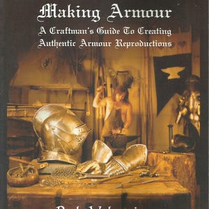 May include: Book cover titled "The Art Of Making Armour" with text "A Craftsman's Guide To Creating Authentic Armour Reproductions" and author "Rob Valentine". The image shows a blacksmith at work, with armor pieces on a wooden table.