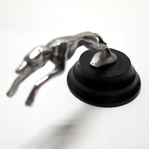 May include: A silver Greyhound figurine leaping forward, mounted on a black wooden base.