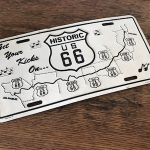 May include: White metal license plate with a black and white map of Route 66, with the text "Get Your Kicks On... Historic US 66" and "Los Angeles" and "Chicago".