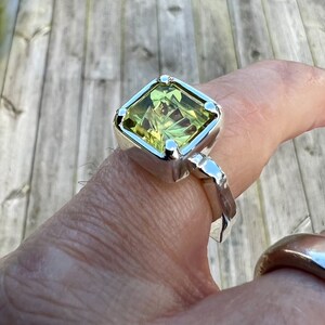 Peut inclure: Une bague en argent avec une grande pierre pr&eacute;cieuse carr&eacute;e verte. La bague a une bande textur&eacute;e.