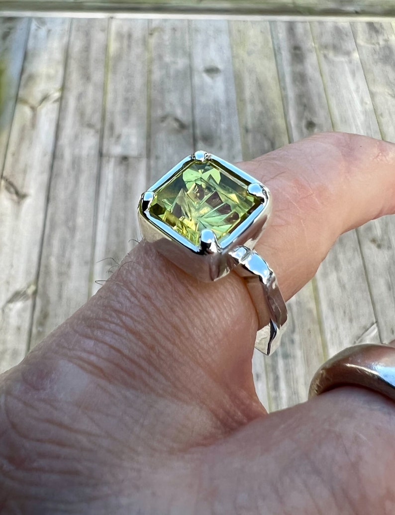 Peut inclure: Une bague en argent avec une grande pierre pr&eacute;cieuse carr&eacute;e verte. La bague a une bande textur&eacute;e.