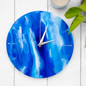 May include: A blue and white resin clock with silver hands. The clock face has a swirling, abstract design.