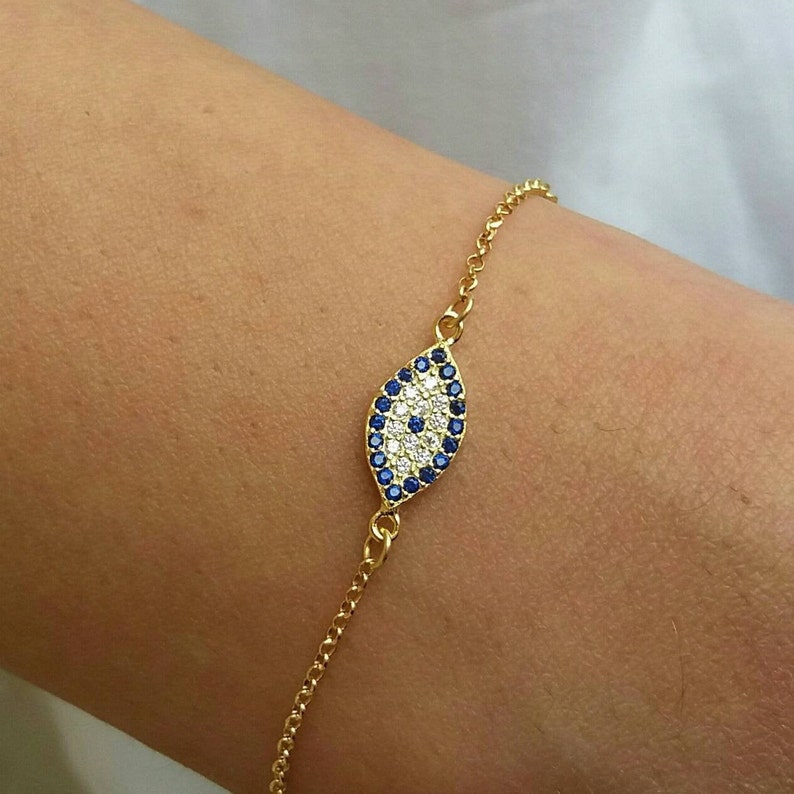 Model wearing a Dainty bracelet with evil eye pendant with cubic zirconia clear in the middle and blue around. The chain is 14k gold filled 0,8mm. The bracelet is delicate, and is protecting the person that is wearing it.