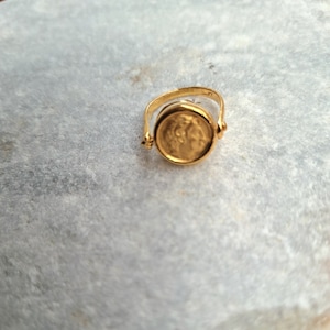 May include: A gold ring with a spinning coin design. The coin features a profile of a person's face.