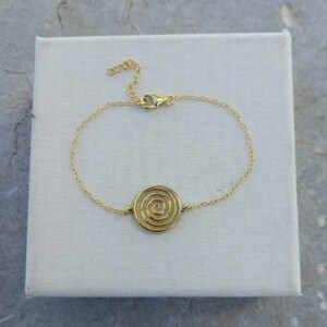 May include: A gold chain bracelet with a circular pendant featuring a spiral design.