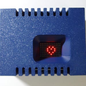 May include: A blue, textured, rectangular box with a red LED display in the center. The display shows a heart shape.