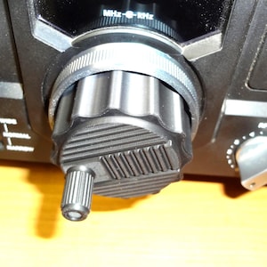 May include: Close-up of a black radio control panel with a large, textured tuning knob. The knob has a ridged edge and a smaller, cylindrical extension. The panel also features a smaller silver knob and text indicating frequency settings.