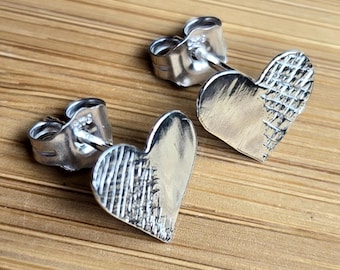May include: A pair of silver heart-shaped stud earrings with a textured design on one side of each heart.
