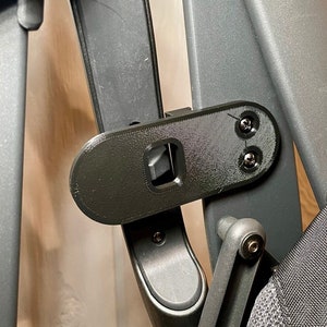 Puede incluir: Primer plano de un marco de cochecito negro con un tornillo plateado. El marco está hecho de metal y tiene un acabado texturizado.