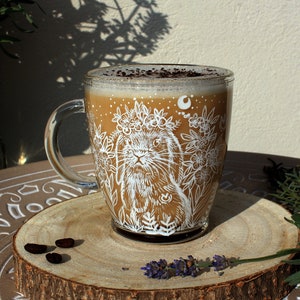May include: A white ceramic mug with a floral design and a rabbit wearing a flower crown. The mug is filled with a brown liquid and has a white rim. The mug is sitting on a wooden coaster.
