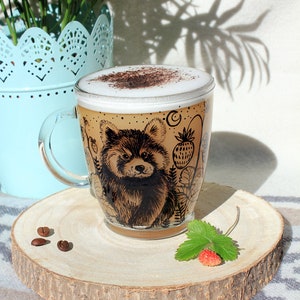 May include: A clear glass coffee mug with a red panda design, filled with a cappuccino. The mug sits on a wooden coaster with coffee beans and a strawberry. A light blue planter and green plants are in the background.