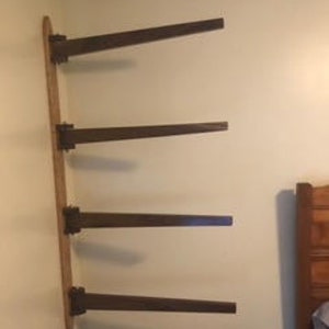 Puede incluir: Una estantería de madera montada en la pared con cuatro estantes. Los estantes son de madera marrón oscuro y están fijados a una pared blanca. Los estantes están vacíos.