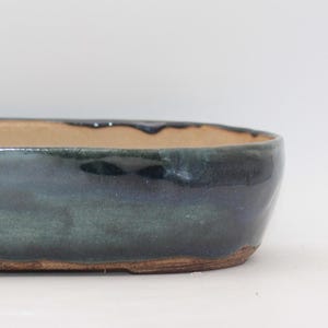 Peut inclure: Un pot à bonsaï ovale en céramique avec un extérieur recouvert d'une glaçure brillante bleu-vert profond. L'intérieur et la base du pot présentent une finition en argile beige naturelle non émaillée, avec un bord arrondi et un profil bas.