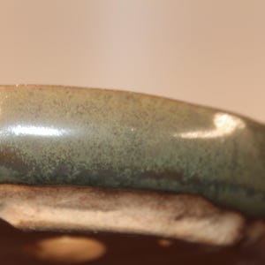 Könnte beinhalten: Nahaufnahme des oberen Rands eines Keramik-Bonsai-Topfs. Der Topf ist dunkelgrün mit einer gesprenkelten Glasur. Der Rand des Topfes ist leicht erhöht und hat eine hellbraune Farbe.