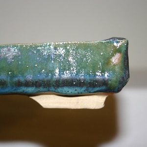 May include: A close-up of the edge of a green and blue ceramic planter with a speckled glaze. The planter has a slightly irregular shape.